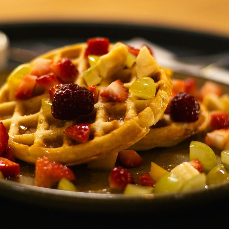 Waffles de baunilha feitos na casa finalizados com frutas frescas do dia e mel.