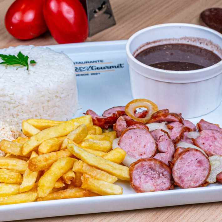 Linguiça Toscana com fritas, acompanhado por um arroz branco soltinho, um feijão caseiro repleto de sabor, farofa crocante. Todos esses itens são servidos em uma prática marmita com aproximadamente 600gr, nossa embalagem vai ao microondas.