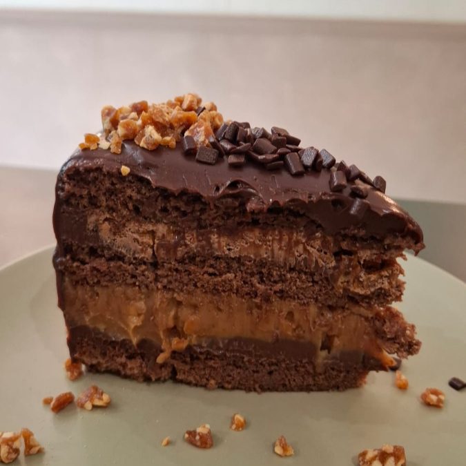 Pão de ló de chocolate, ganache com blend de chocolates, caramelo cremoso com amendoim, nougat com crocante de amendoim, finalizado com ganache de chocolate, pedaços de charge e crocante de amendoim.