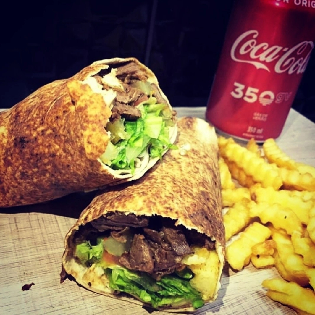 Experimente nosso Shawarma de Carne: finas tiras de carne temperadas e grelhadas, alface crocante, tomate fresco, batatas fritas douradas e picles saborosos, tudo envolvido por pasta de alho cremosa. Acompanha pote extra de pasta para intensificar cada mordida.
