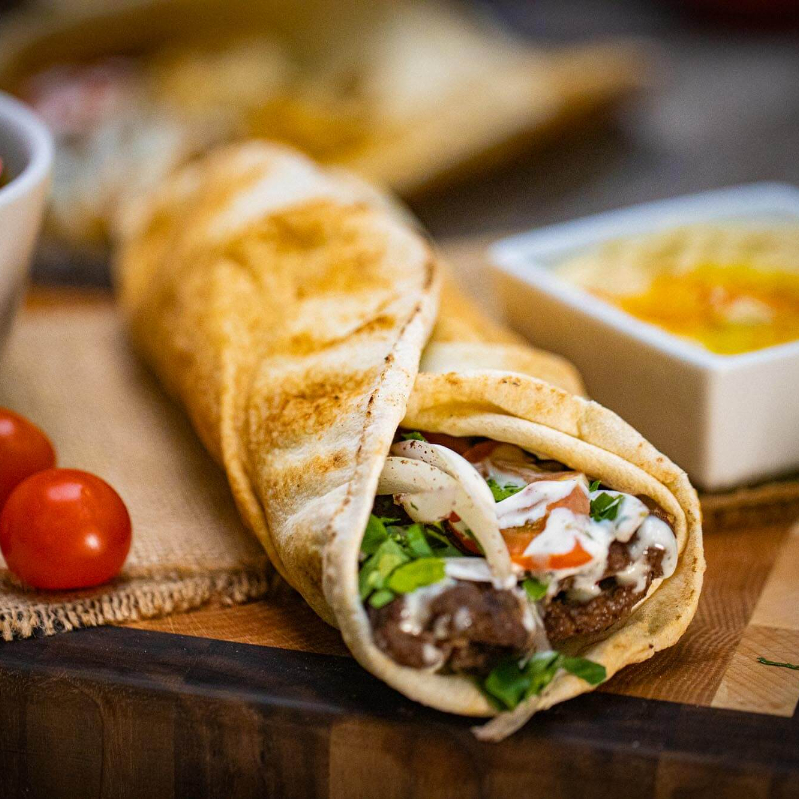 Experimente nosso Kebab de Carne: finas tiras de carne temperadas e grelhadas, salada de repolho, batatas fritas douradas e picles saborosos, tudo envolvido por pasta de alho cremosa. Acompanha pote extra de pasta para intensificar cada mordida.