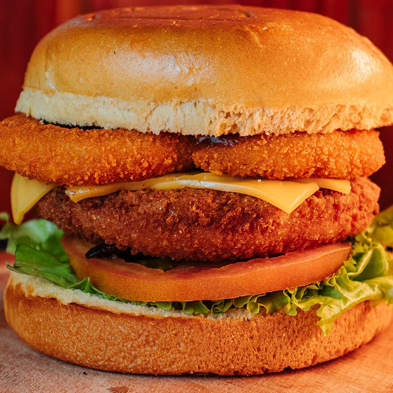 Black Chicken Burger: hambúrguer de frango empanado crocante, queijo prato, alface, tomate, cebola empanada, maionese da casa e molho mostarda e mel, tudo no pão de brioche. Uma combinação irresistível de sabores e texturas!