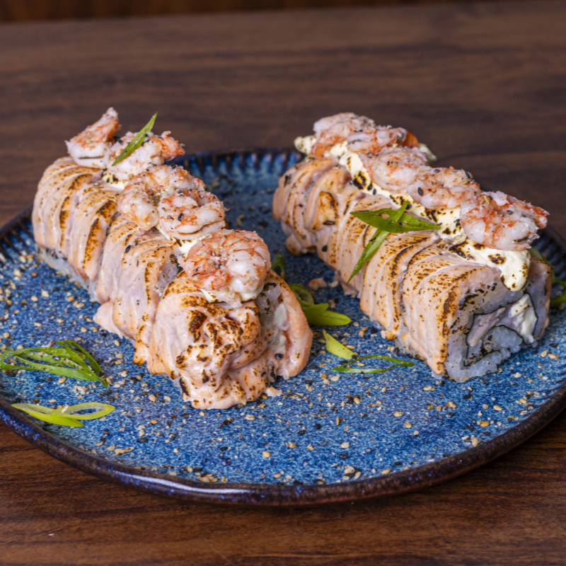 Arroz enrolado no nori com recheio de de salmão e cream cheese. Por cima, tirinhas de salmão com camarões empanados.