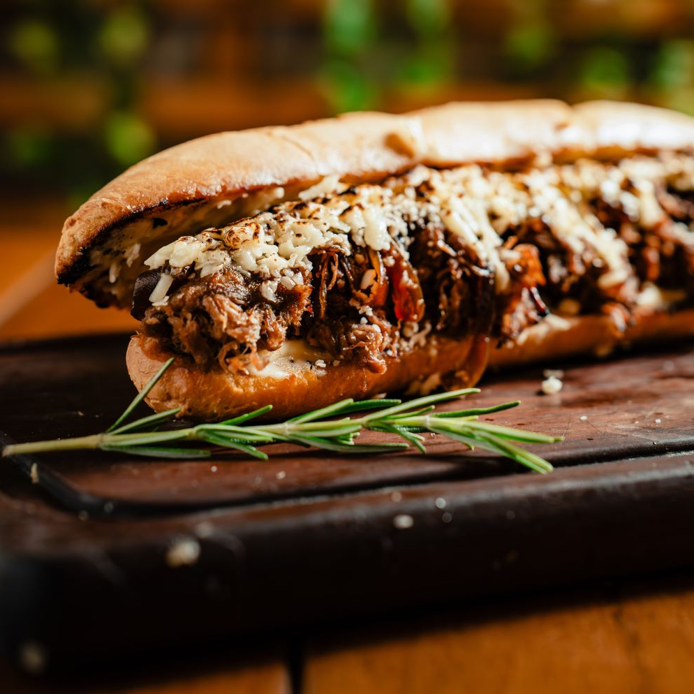 Baguete, costela desfiada, catupiry, queijo gratinado, molho chimichurri e cebola caramelizada