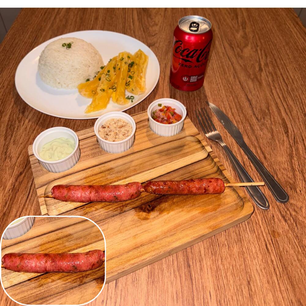 Espeto de linguiça (fininha de porco) acompanhado por arroz, mandioca, vinagrete, farofa crocante e molho verde.