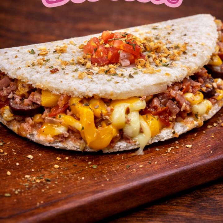 Uma Das Mais Pedidas! Diretamente da Feira Nacional do Podrão para o seu prato, a Tapi Tudo da Ari é um verdadeiro espetáculo de sabor! Uma Mega tapioca recheada com calabresa suculenta, presunto saboroso, cheddar cremoso, requeijão derretido, mussarela puxa-puxa, bacon, ovos de codorna, cebola, tomate fresquinho, orégano perfumado e alho torrado crocante! Se você gosta de uma tapioca bem recheada e cheia de sabor, essa é pra você! Peça agora e descubra por que ela fez tanto sucesso! ️