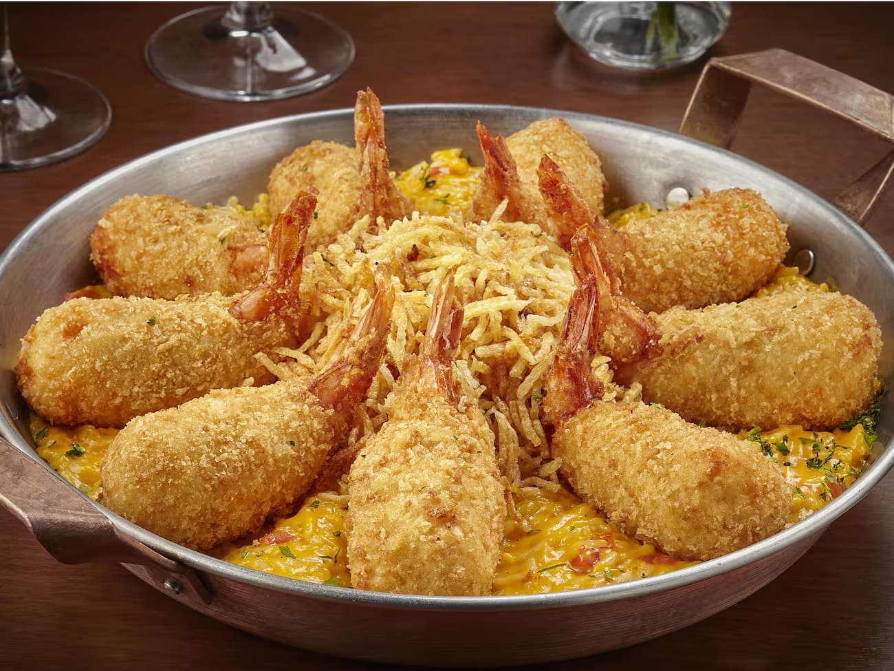 9 Camarões empanados recheados com Catupiry, coentro servidos sobre cremoso arroz com camarões e molho de moqueca. Servido com batata palha e farofa de pão.