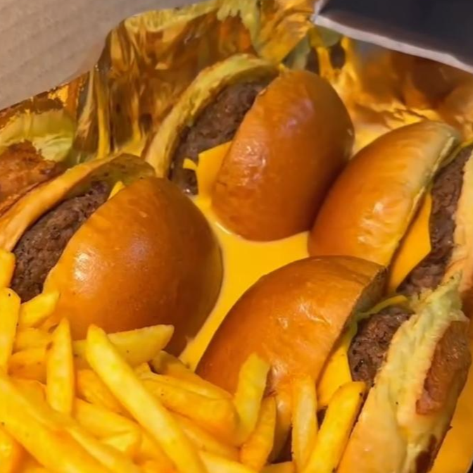 2 x-burguer partidos ao meio mergulhados no cheddar com batata frita e farofinha de bacon finalizando