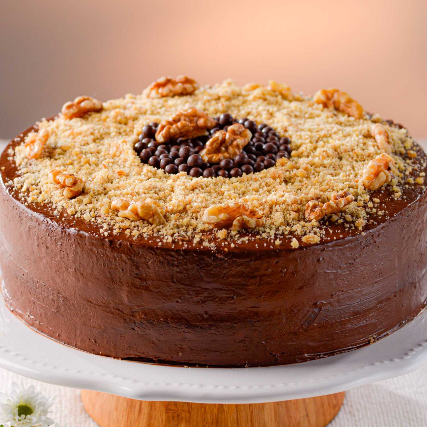 Delicioso Bolo de nozes caseiro, com de recheio de brigadeiro, coberto com calda de chocolate, decorado com bolinhas de chocolate e nozes trituradas. Imagem meramente ilustrativa.