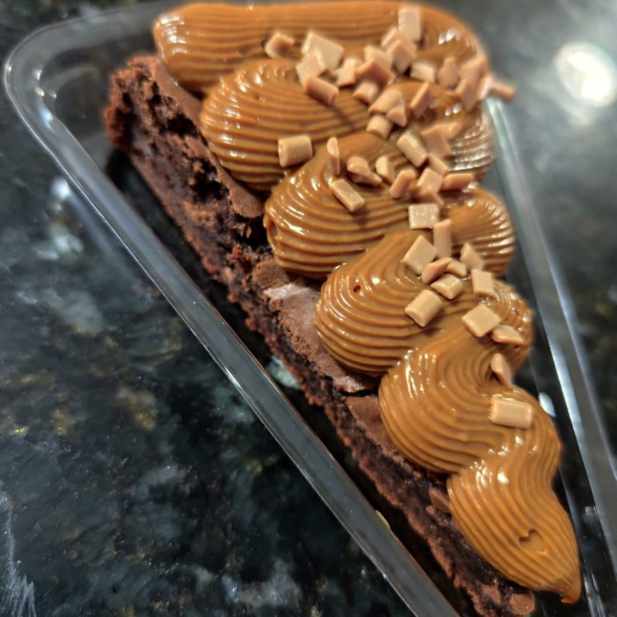 Fatia do nosso brownie com uma massa bem chocolatuda e uma leve casquinha crocante por fora. Generosa cobertura de doce de leite cozido na panela de pressão e finalizado com granulado de caramelo nobre.