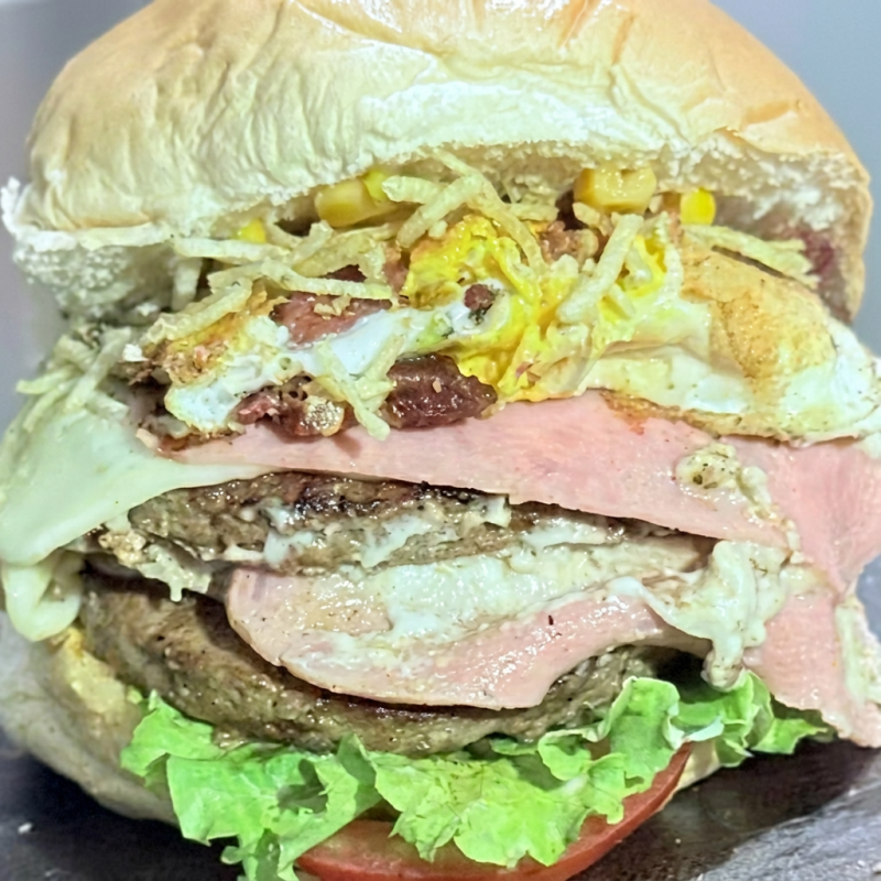 Pão, 2 Hambúrgueres de Picanha de 120g, 2 Presuntos, 2 Queijos, Ovo, Bacon, Frango Desfiado, Catupiry, Milho, Batata Palha, Salada de Alface e Tomate e o Molho da Casa.