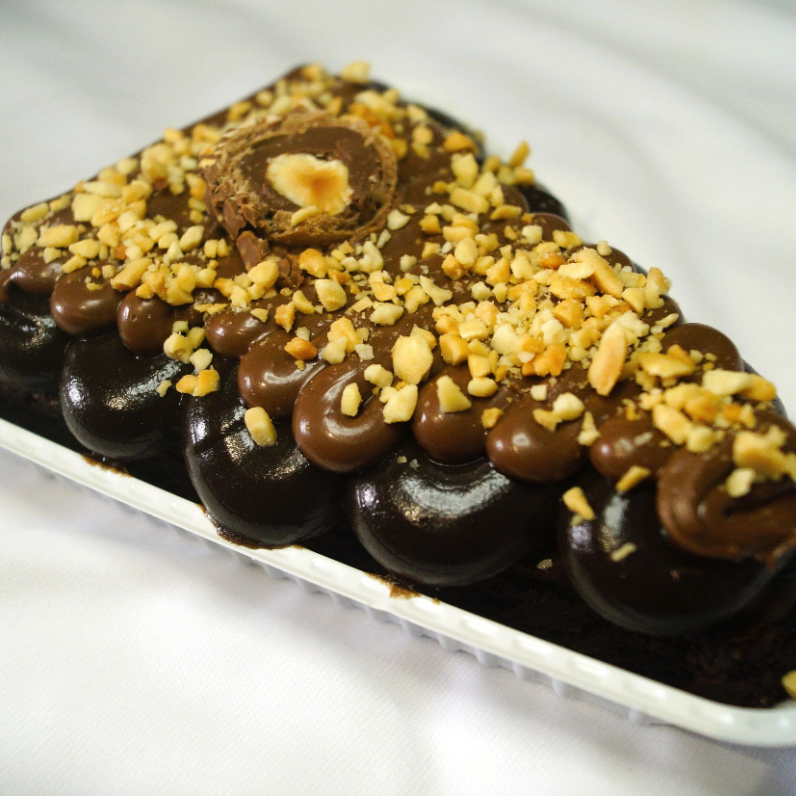 Brownie com cobertura de brigadeiro meio amargo e Nutella, decorado com amendoim triturado e metade de um Ferrero Rocher. Um sabor sofisticado, intenso e irresistível.