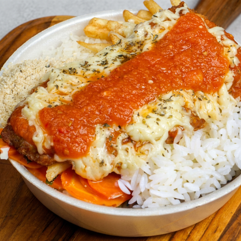 Apresentamos nossa irresistível 'Marmita Frango à Parmegiana', um prato da categoria 'Marmitas'. Delicie-se com um suculento filé de frango, generosamente gratinado à parmegiana, acompanhado de um arroz soltinho e bem temperado. Incluímos também nosso refogado do Dia, que pode ser uma nutritiva couve ou um saboroso repolho, entre outras opções. Além disso, você tem a liberdade de escolher entre crocantes batatas fritas, um cremoso purê ou a clássica batata palha para completar sua refeição. Uma combinação que promete satisfazer seu paladar!