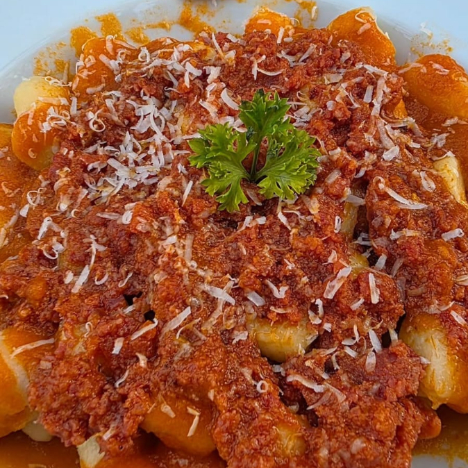 Nhoque de batatas com ragu de linguiça Blumenau, servido com molho vermelho