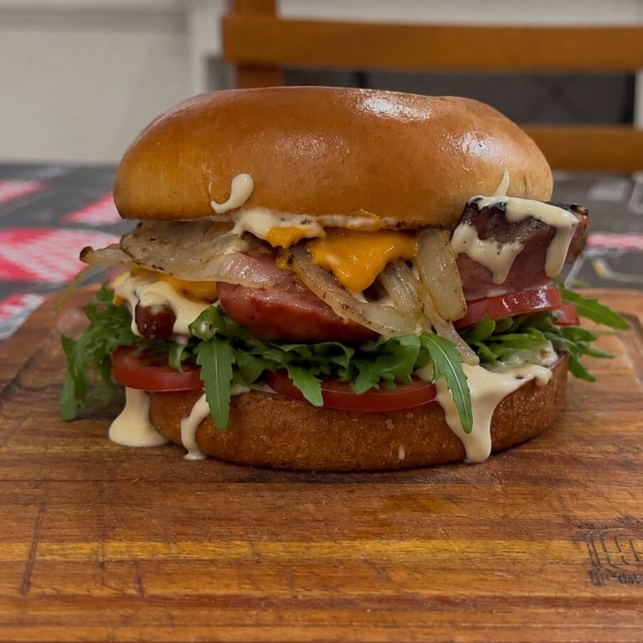 pao brioche, calabresa defumada, queijo cheddar fatiado, cebola na chapa, maionese de parmesao e rucula