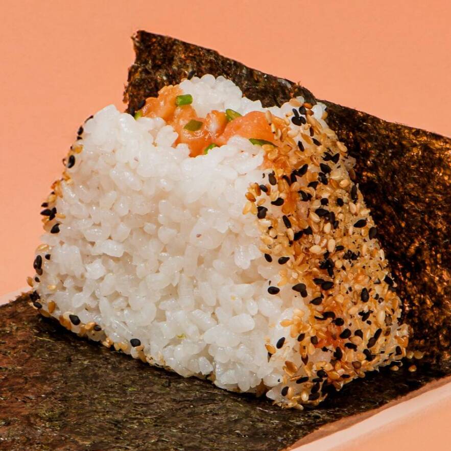 Bolinho de arroz Shari, recheado com salmão, raspas de limão, azeite trufado e cebolinha, envolto por um mix de gergelim e acompanhado de alga nori, embalada separadamente para manter a crocância até o momento de consumo.