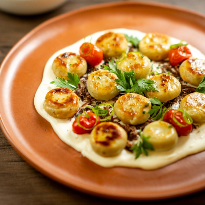 Nhoque assado de batata doce com carne de sol desfiada e creme de nata.