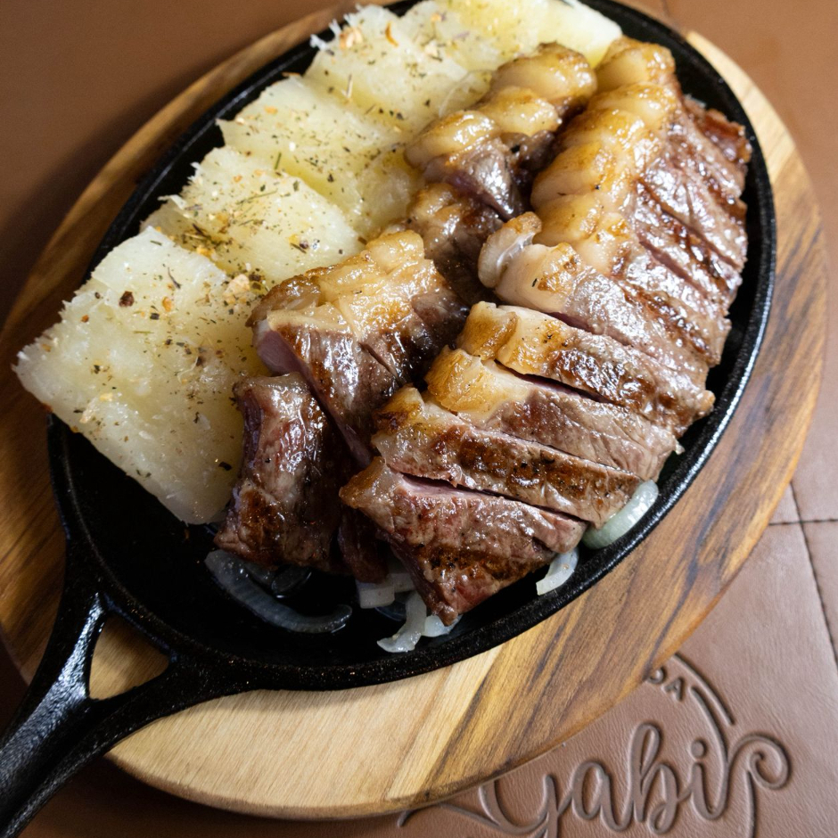 A princesinha do churrasco, servida sobre uma cama de cebolas e acompanhada de mandioca temperada da casa