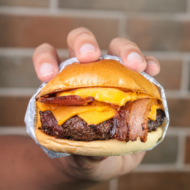 Pão brioche selado na manteiga, com suculento blend bovino de 180g, bacon, molho cheddar artesanal, queijo cheddar derretido e cebola roxa.