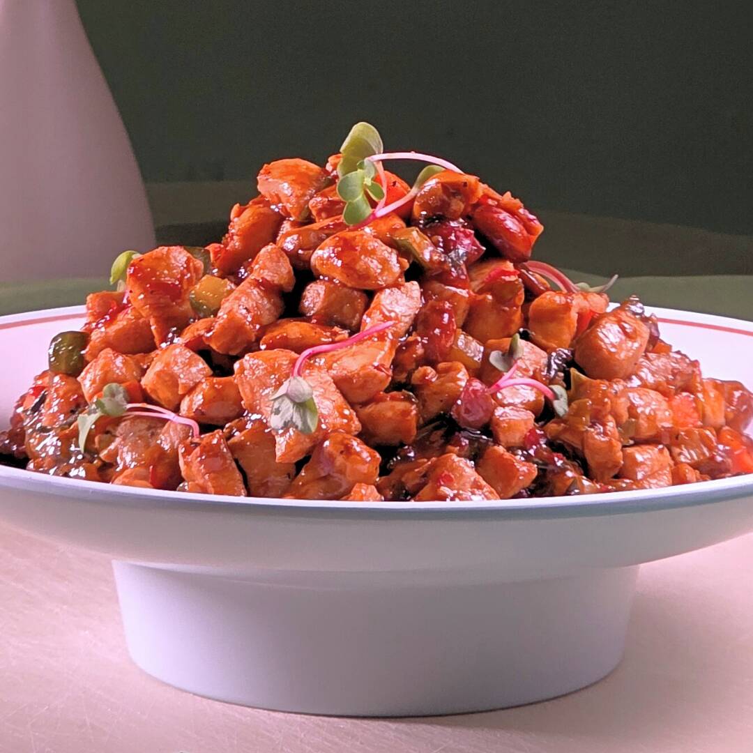 Conhecido no Ocidente como Frango Xadrez. Cubos de frango salteados com pepino, cenoura, cebolinha, amendoim e castanha de caju, em molho agridoce e picante.