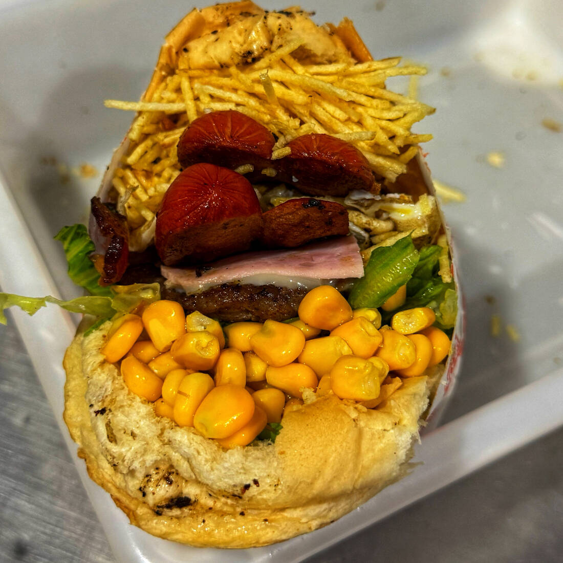 Pão, hambúrguer, bacon, salsicha, ovo, presunto, mussarela, alface, milho e batata.