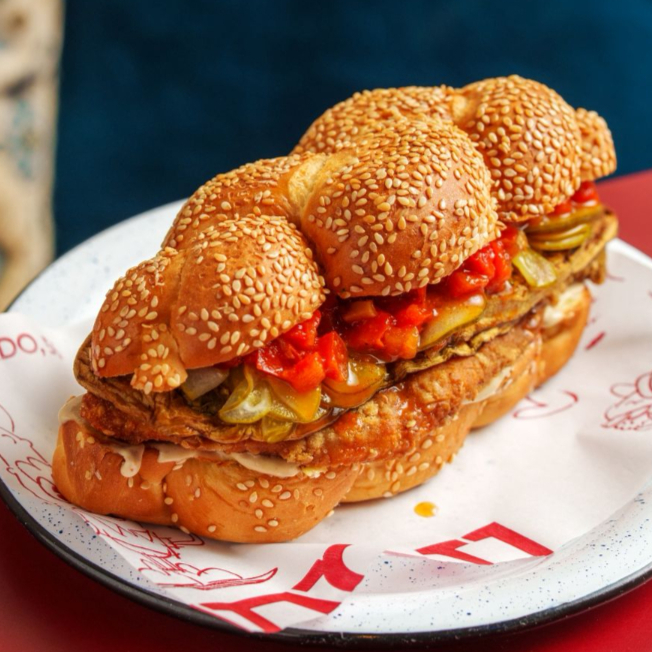 Filé de frango empanado com gergelim, tehina, matbucha, berinjela grelhada e picles de pepino.