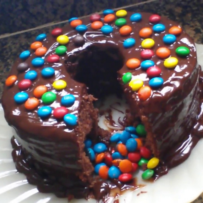 Bolo massa de chocolate com cobertura de chocolate e confeites por cima.