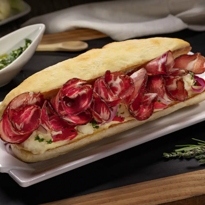 Sanduiche com copa fatiado, pão ciabatta, picles de cebola, rúcula e molho