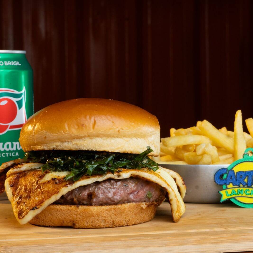 Escalação oficial: Brasil – Edição Exclusiva Da Copa Do Mundo!
O dono da casa entrou em campo para golear a sua fome! Uma receita com a nossa alma, criada em edição super limitada e disponível apenas durante a Copa do Mundo.
Prepare-se para o verdadeiro sabor do nosso país: um suculento hambúrguer artesanal combinado com o toque tostado do queijo coalho com orégano, a crocância irresistível da couve frita e o aroma marcante do alho torrado. Tudo isso servido no pão da copa. É a nossa seleção em forma de burger!
Brinde Colecionável: Garanta o manto do seu estômago e leve na faixa um Chaveiro personalizado do Cartoon Lanches!
️ Não deixe para a prorrogação! Esse sucesso é limitado e vai sair de campo assim que a Copa acabar.