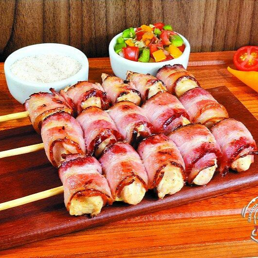 Cubos de frango enrolando com tiras de bacon