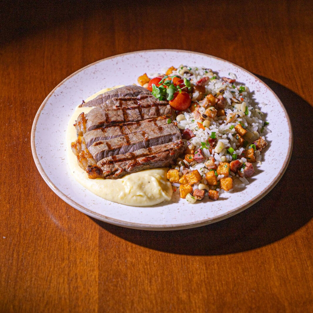 Carne de sol fatiada, acompanha purê de mandioca e arroz baião de dois.