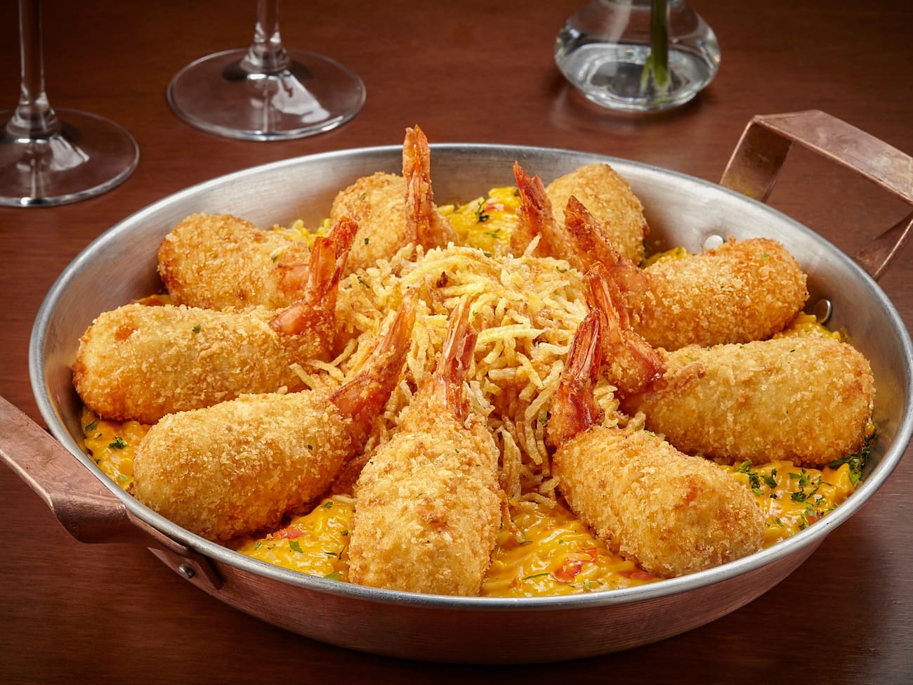 9 Camarões empanados recheados com Catupiry, coentro servidos sobre cremoso arroz com camarões e molho de moqueca. Servido com batata palha e farofa de pão.