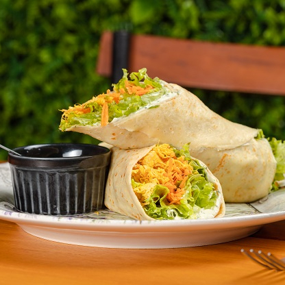 Wrap leve recheado com mix de folhas, cenoura fresca, tomate, frango desfiado e pasta de ervas, combinando frescor, proteína e sabor equilibrado para uma refeição leve e nutritiva. Proteína 100g