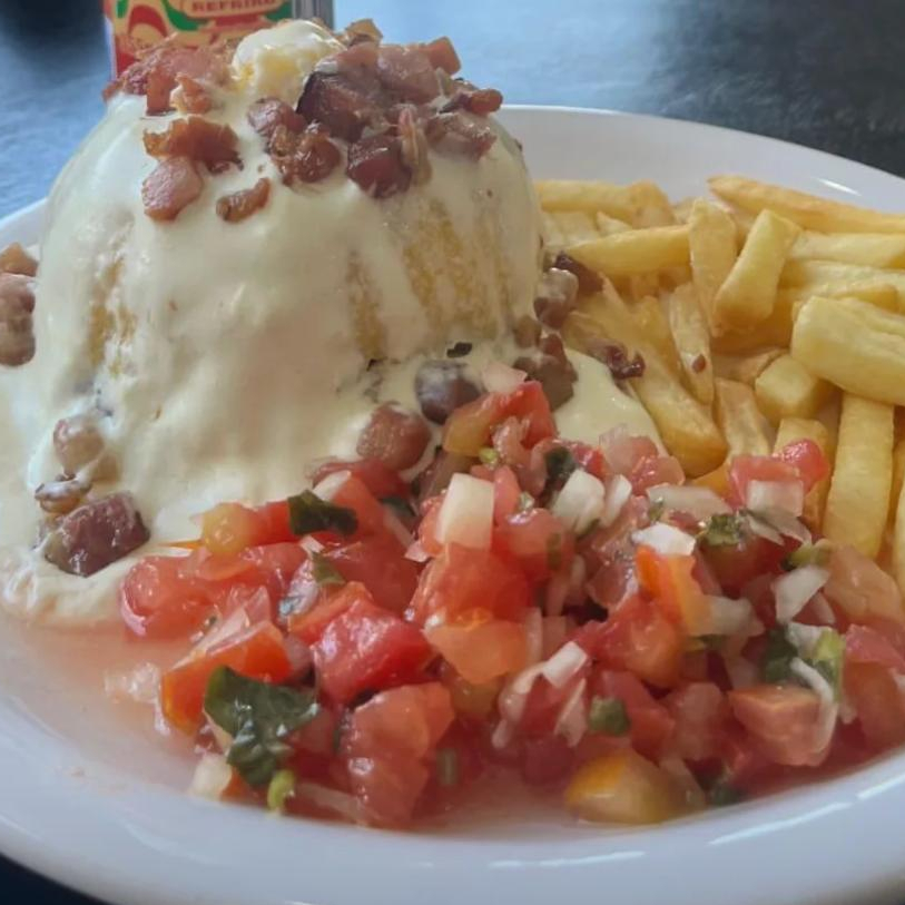Cuscuz recheado com carne seca, coberto com creme de queijo, acompanha vinagrete, bacon e batata frita
