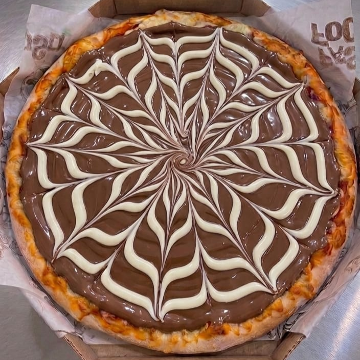 Chocolate com avelã e chocolate branco derretendo juntos com mussarela sobre massa artesanal. Dois amores em cada fatia.