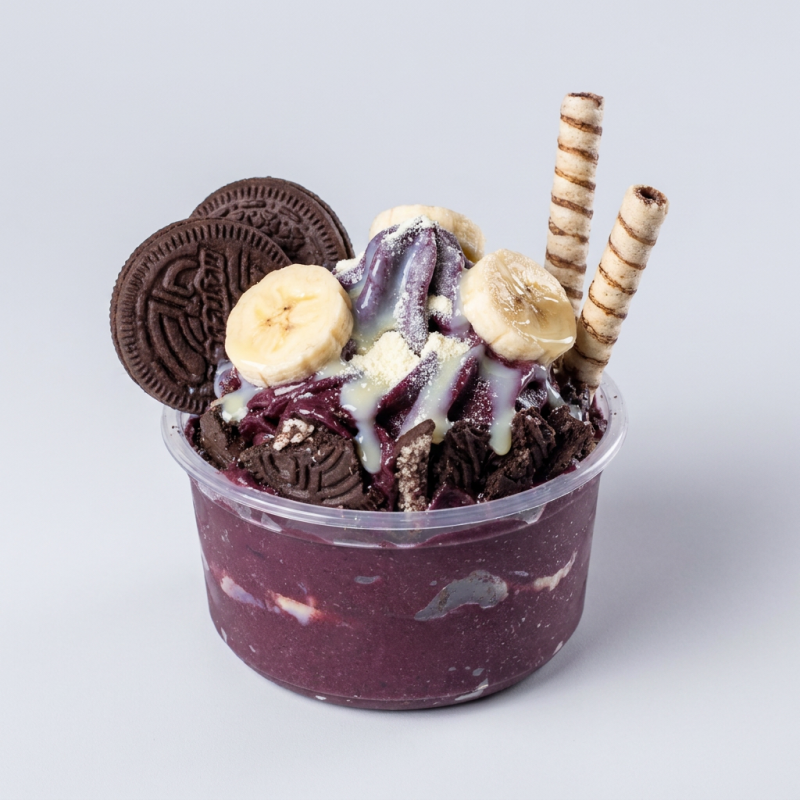 Creme de açaí acompanhado de banana, leite condensado, leite em pó, Oreo granulado e Ovomaltine no pote, e mais tubetes.