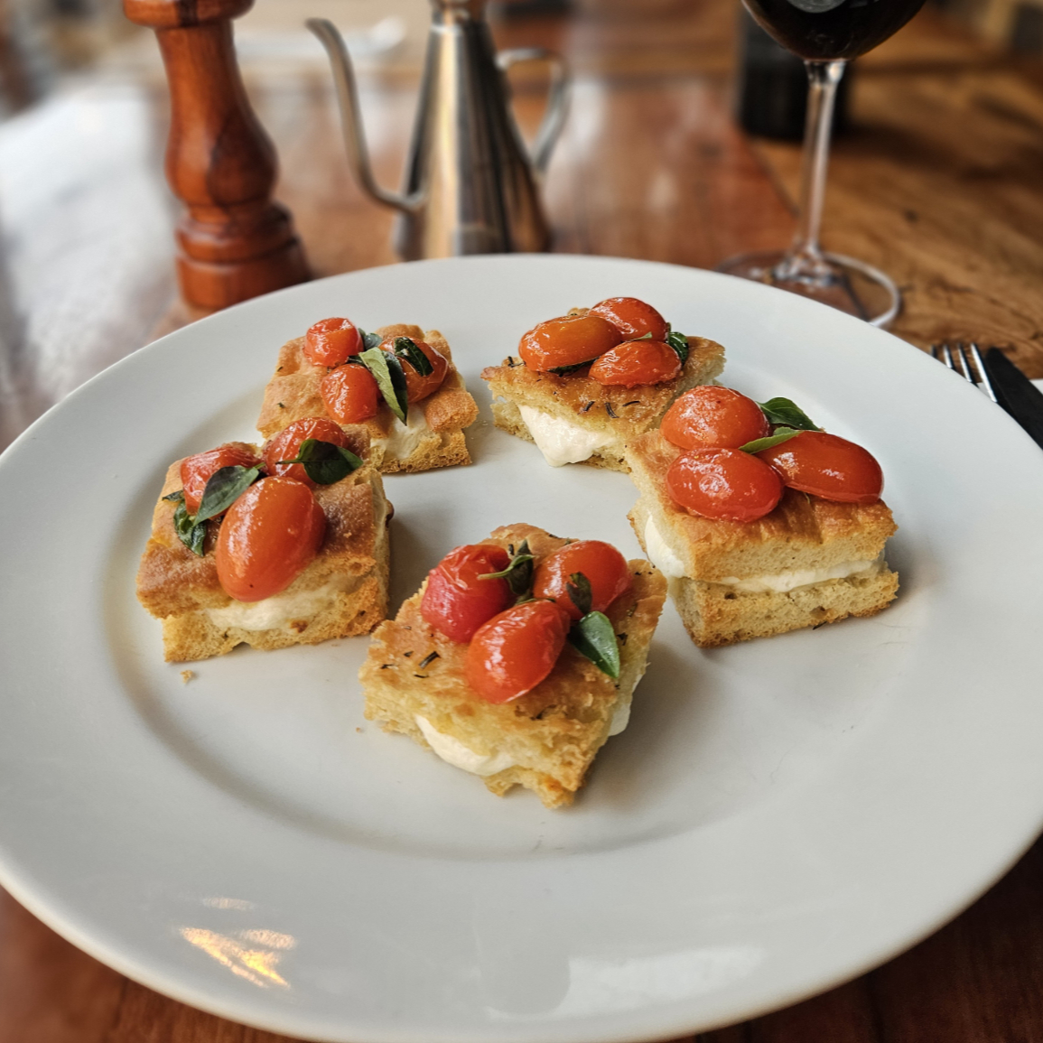 Focaccia recheada com stracciatella, coberta com tomates cereja puxados no azeite de oliva com manjericão fresco. (Prato Vegetariano)