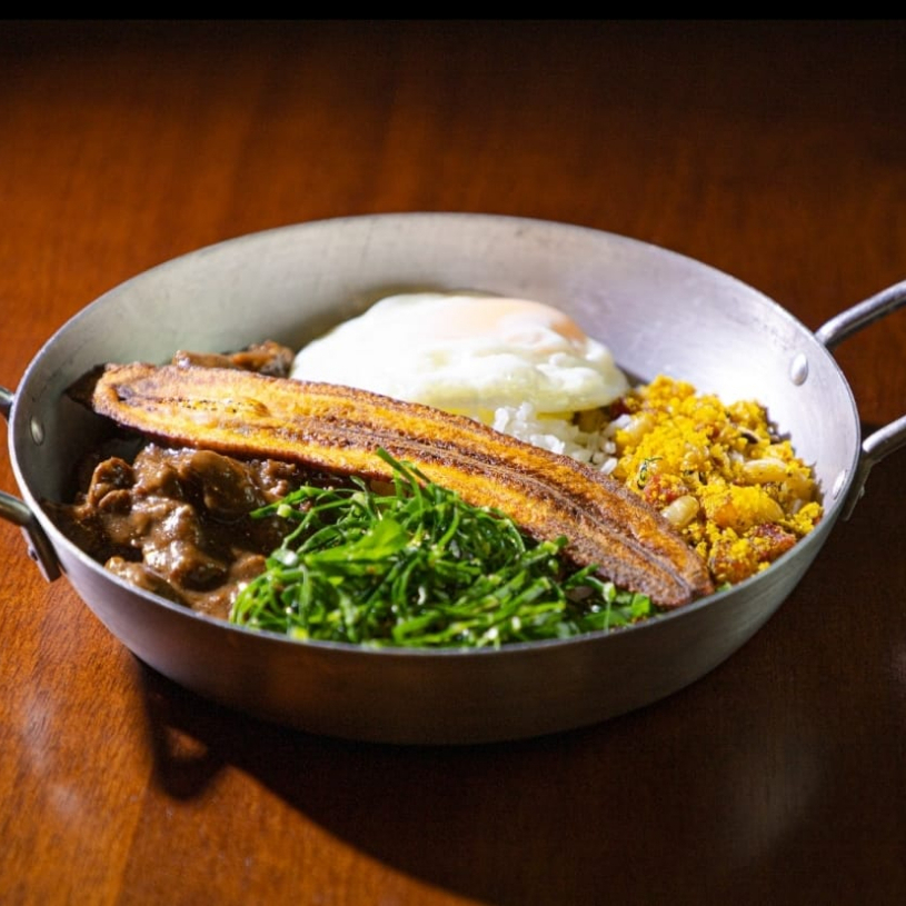Picadinho de Filé, acompanha arroz branco, farofa baiana (bacon, banana da terra, feijão fradinho e coentro), couve refogada, ovo frito e chips de banana da terra.