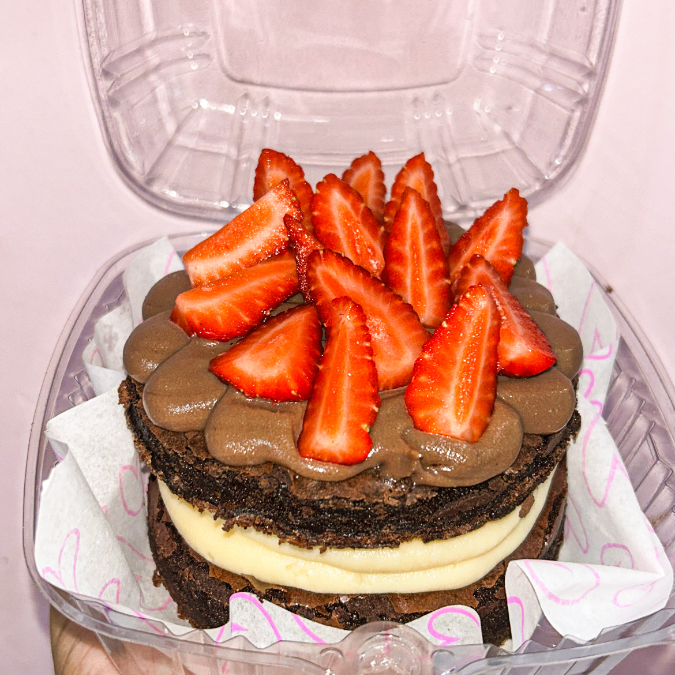 Um super brownie (2 rodelas de 10cm cada) recheado com um delicioso creme de ninho no meio, em cima chocolate e lascas de morangos frescos