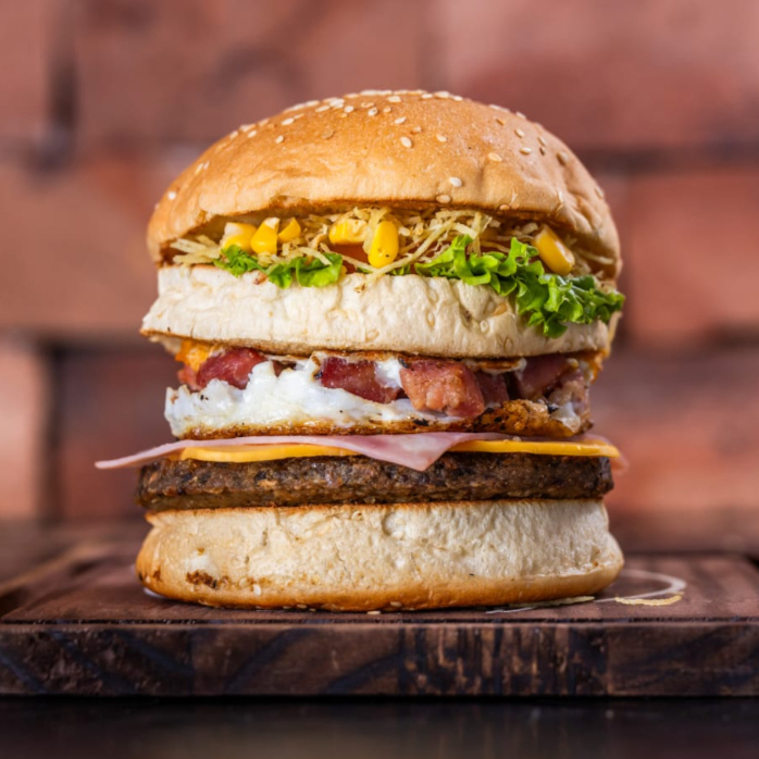 Pão, carne bovina, ovo, bacon em cubos, presunto, queijo prato, milho verde, batata palha, alface e tomate