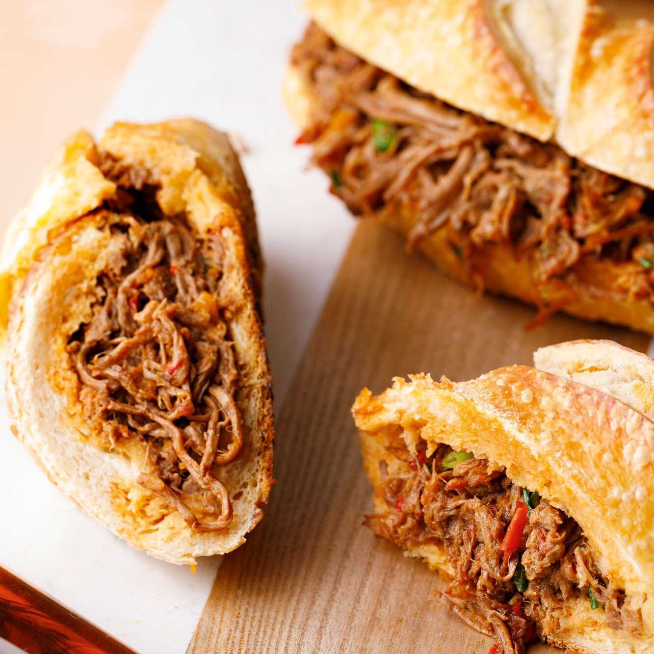 Pão francês crocante recheado com pernil desfiado, cebolas caramelizadas e pimentão crocante, e sirva 1 pessoa.