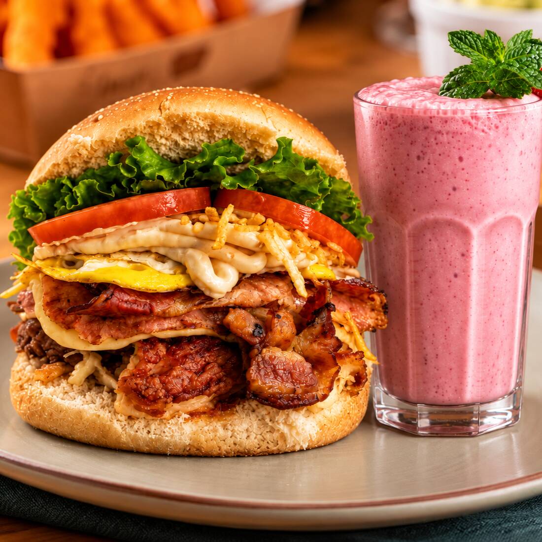 X-Tudo Burguer (pão com burguer bovino (100g), queijo, presunto, bacon, ovos, tomate, alface, milho e batata palha), acompanhado de creme de morango 300ml. Um lanche reforçado com um toque doce para finalizar o pedido.