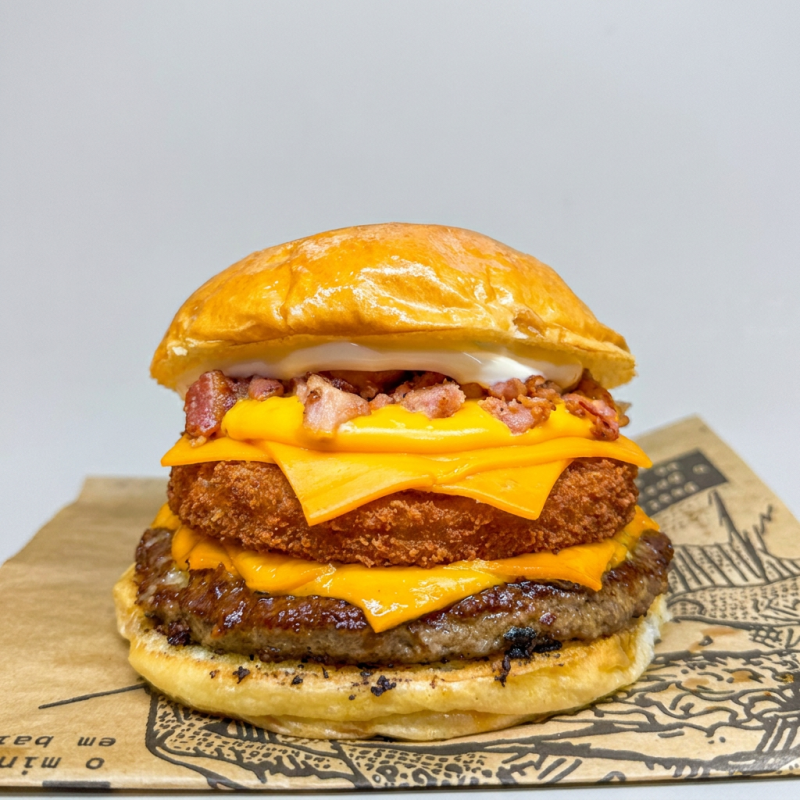 Pão super macio de brioche, 1 burguer artesanal de 120g, 1 burguer de frango crocante, cheddar fatia e cremoso, farofinha de bacon de molho da casa.