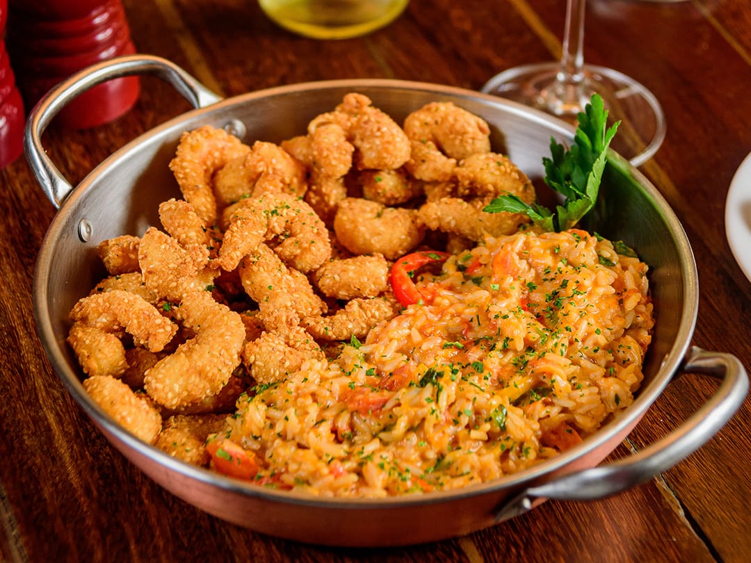 Camarões empanados com gergelim, acompanhados de arroz com leite de coco, molho de tomates frescos, nata, mix de pimentões, cebola, coentro e cebolinha.