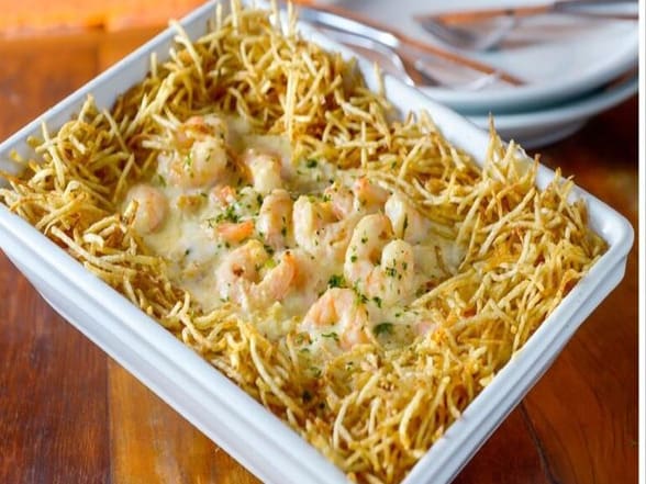 Camarões (18g/cada) servidos sobre cremoso arroz com ervilhas e presunto, envolvidos com molho branco. Gratinado com queijo muçarela. Acompanha batata palha.