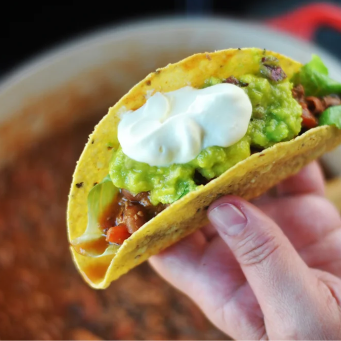 Taco individual recheado com carne moída com chili beans, queijo e para finalizar guacamole.