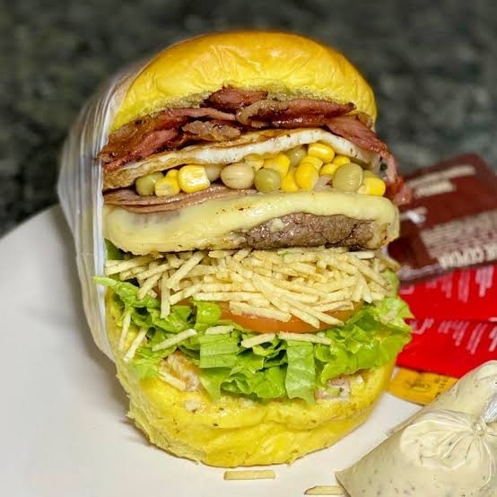 Pão de hambúrguer, 2 carnes, ovo, calabresa, 2x bacon, 2x queijo mussarela, presunto, cheddar, cebola caramelizada, salada.