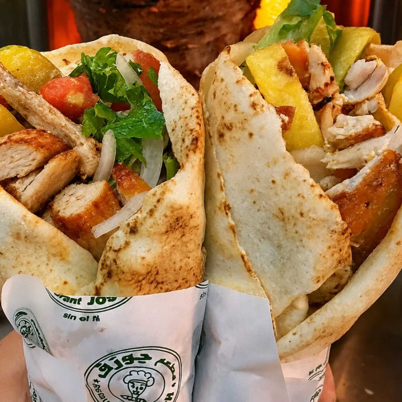Dois shawarmas de frango no pão sírio, preparados com creme de alho, alface, tomate, cebola e batata frita dentro do lanche.