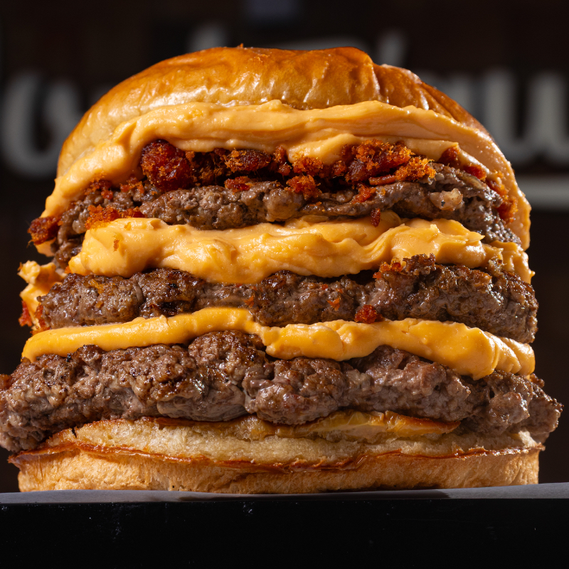 Pão de batata, três blends da casa de 90g (270g), queijo cheddar da casa e farofa de bacon.