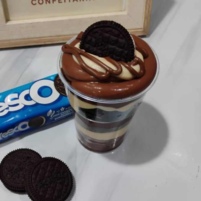 Copo com uma camada de chocolate branco e preto, biscoito negresco e finalizado com Nutella. Serve 1 pessoa.